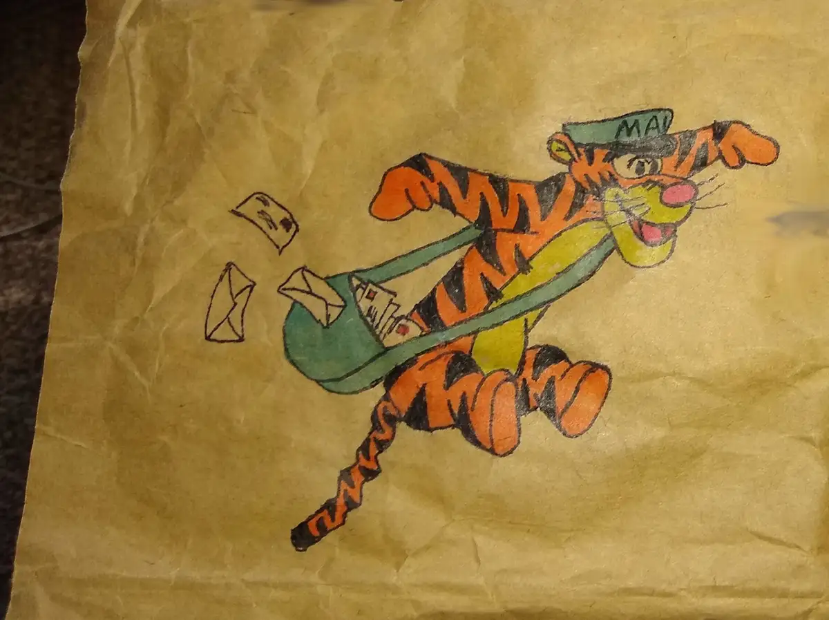 A child's crayon drawing on brown paper shows a cartoon tiger wearing a green hat with 'MAIL' written on it, running while…