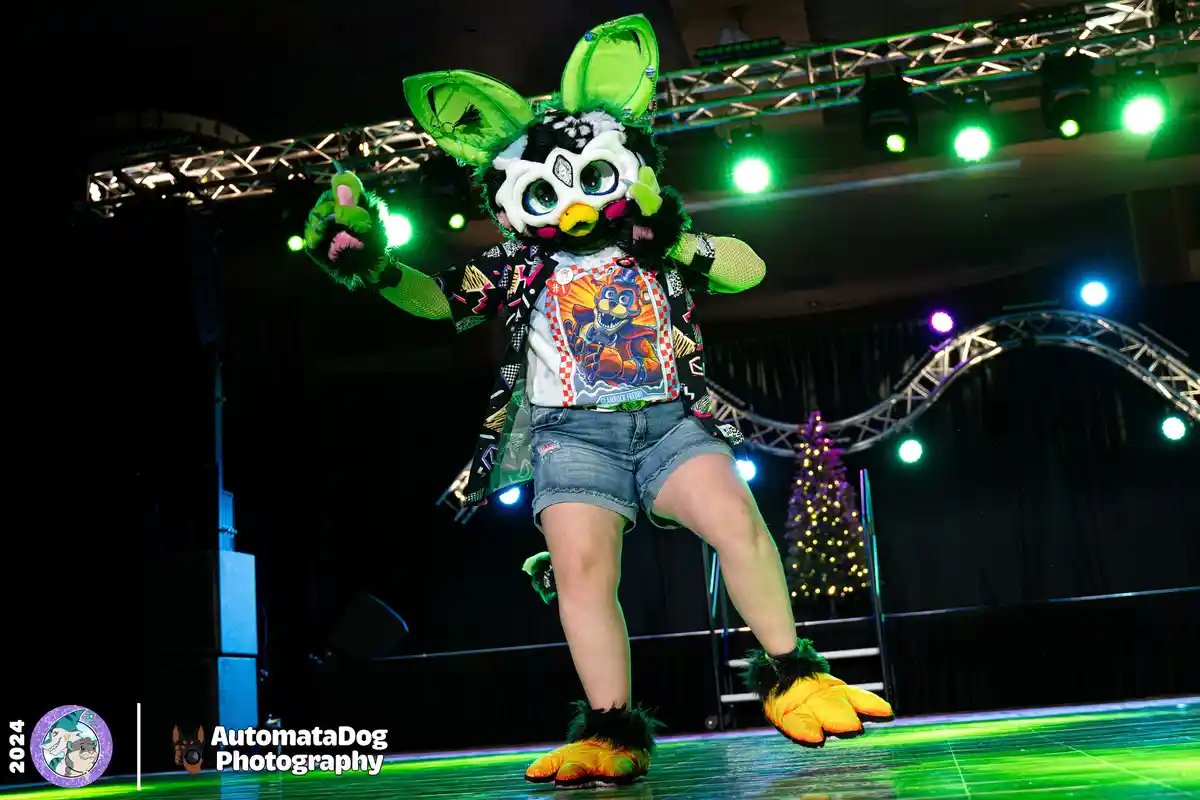 A person in a black and white furry costume with large green ears and a yellow beak stands on a stage under green lights…