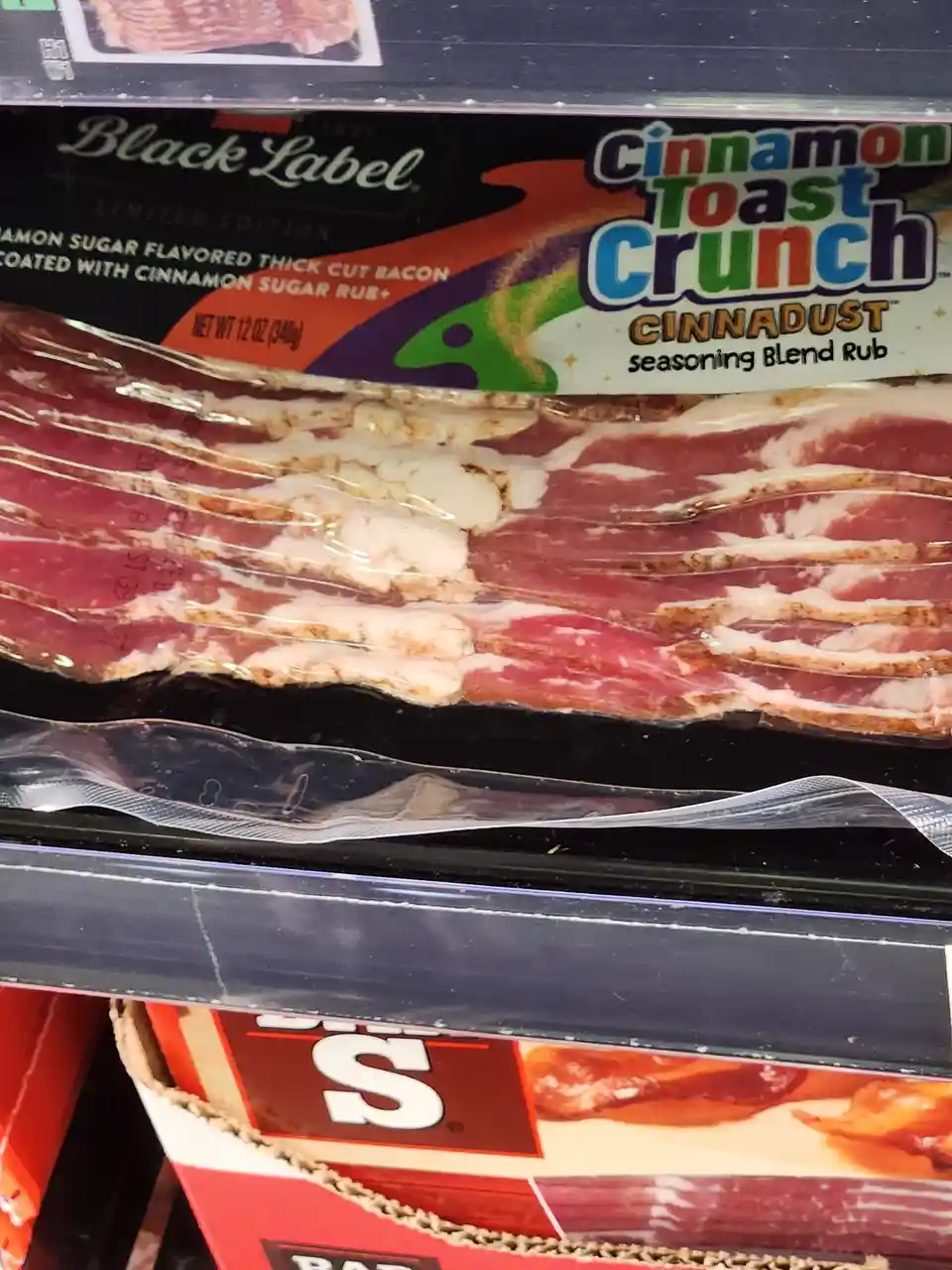 A close-up of a package of Black Label cinnamon sugar flavored thick cut bacon, visibly coated with a seasoning rub, with…
