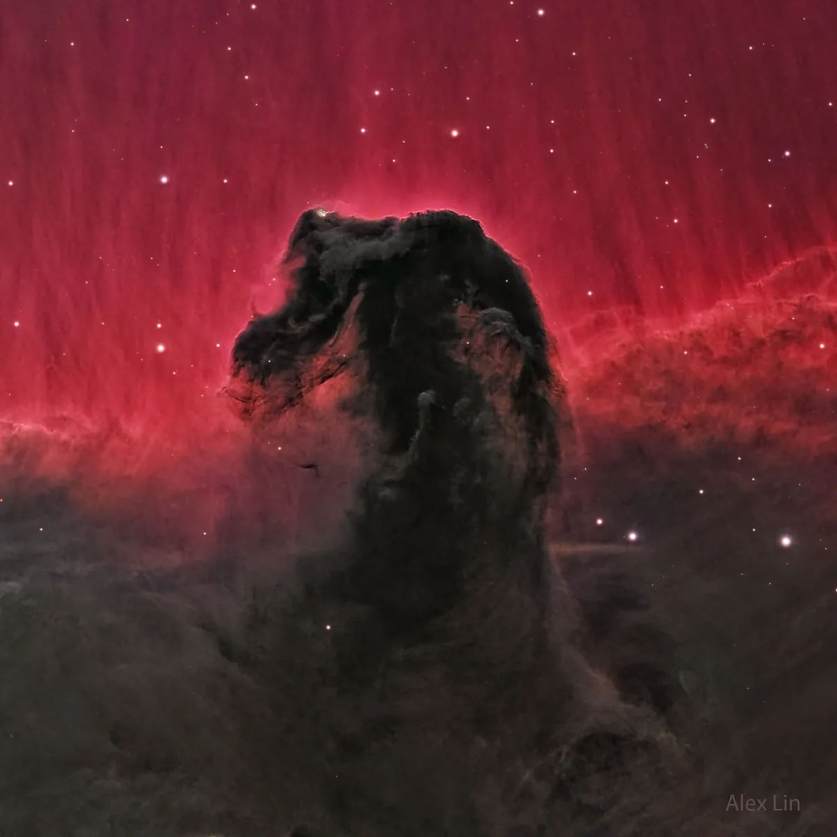 A cosmic nebula image shows a dark, towering pillar of interstellar dust and gas against a vibrant red glowing gas cloud…