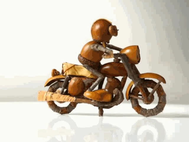 A six-panel image sequence shows a small, intricately crafted wooden motorcycle sculpture rotating 360 degrees on a…