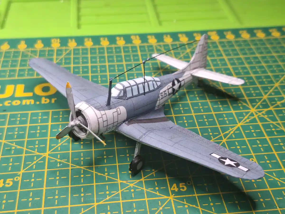 A detailed model of a gray World War II-era U.S. military propeller airplane sits on a green self-healing cutting mat with…