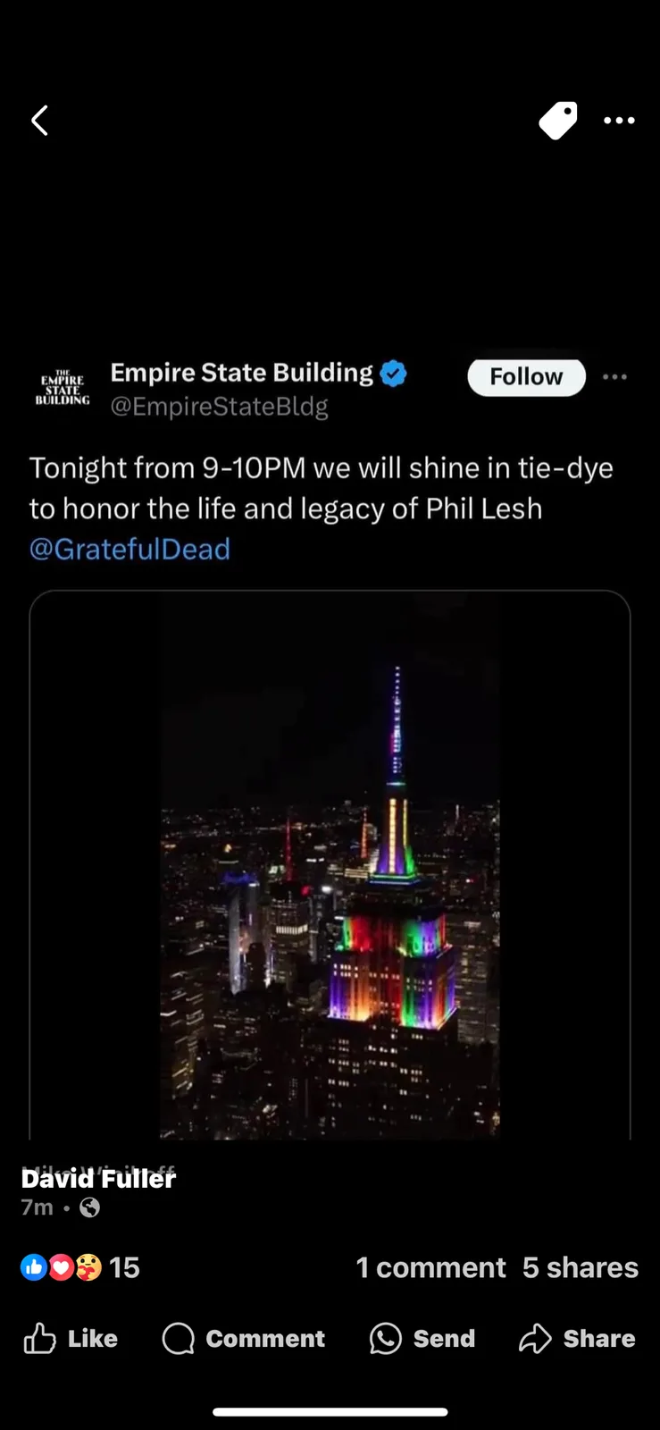 The image shows a nighttime photo of the Empire State Building illuminated with a vibrant, multicolored tie-dye pattern…