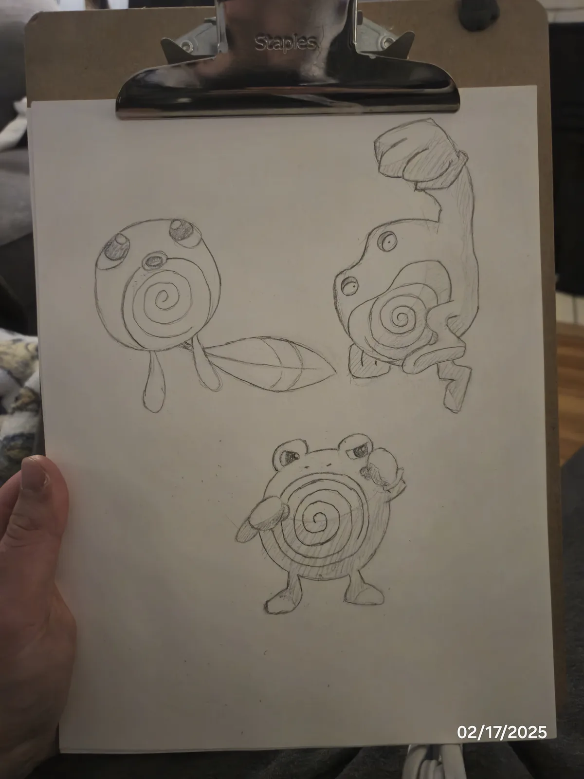 A hand holds a clipboard displaying three pencil sketches of a spiral-shell creature resembling a Pokémon. The top-left…