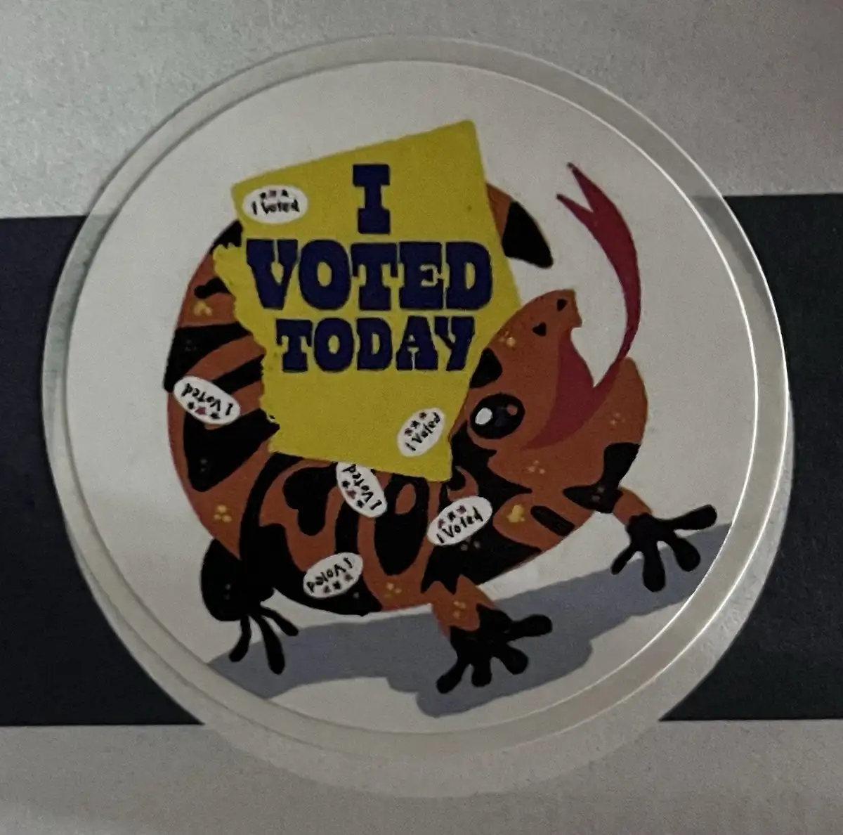 A circular sticker features a cartoonish orange and black striped creature resembling a tiger or cat, holding a large yellow…