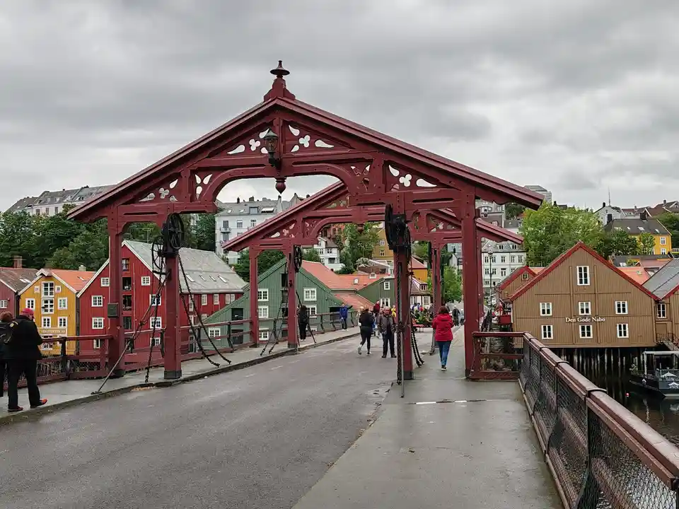 A photo of a red, ornate, drawbridge with people walking across it, set against a backdrop of colorful traditional houses…