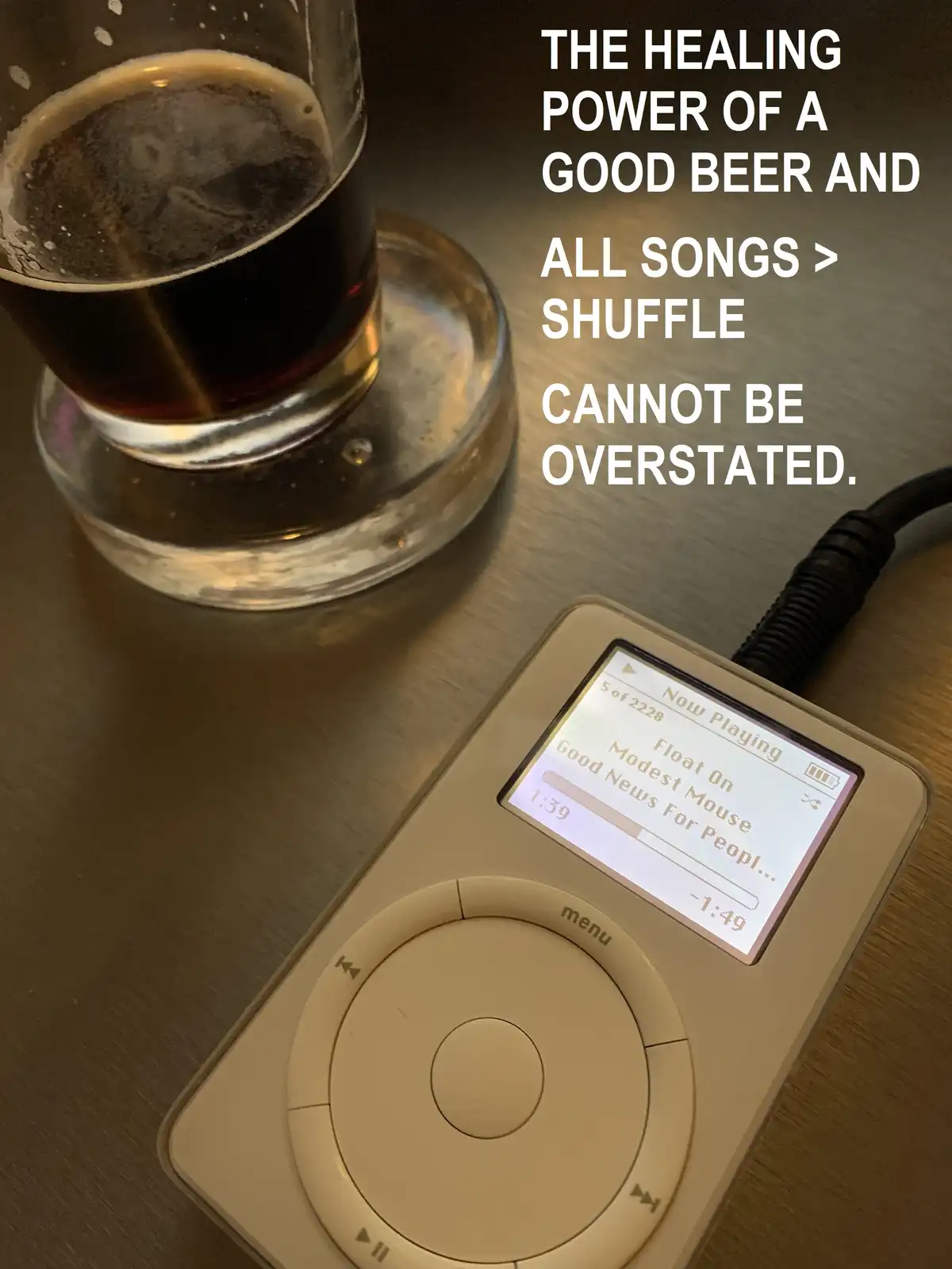 A close-up photo shows a glass of dark beer on a coaster next to a beige iPod Classic playing music. The iPod screen…
