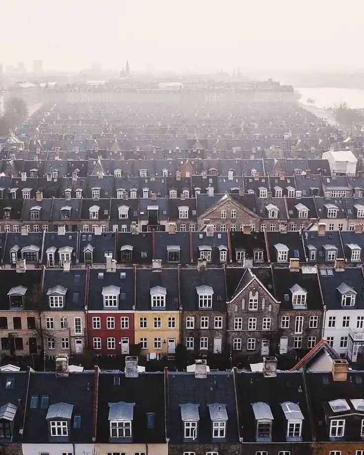 An aerial view of a dense, repetitive urban neighborhood with rows of identical brick houses featuring dark roofs and…