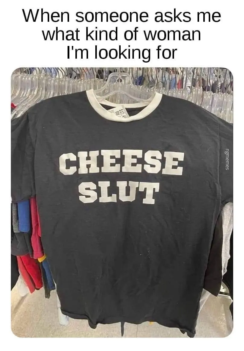A black t-shirt with white block letters reading 'CHEESE SLUT' hangs on a clear plastic hanger in a clothing store aisle…