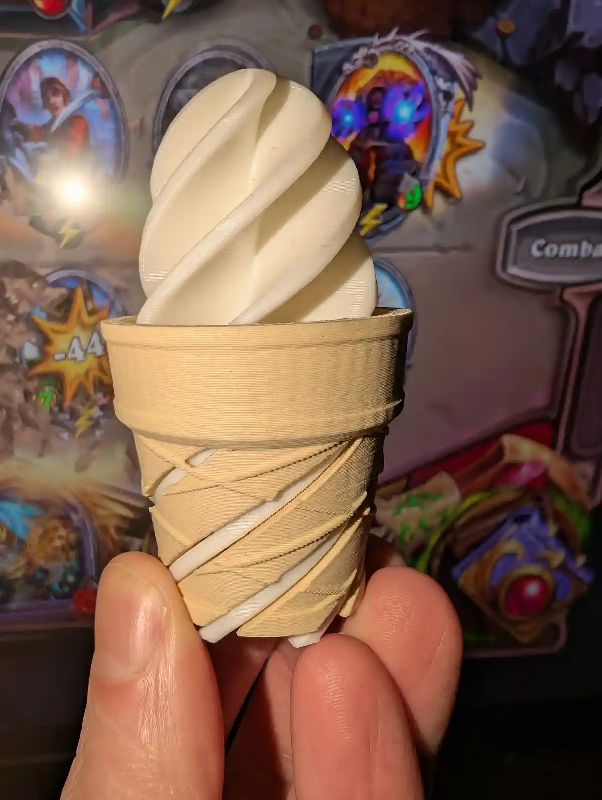 A hand holds a 3D-printed replica of a soft-serve ice cream cone, with visible layer lines on both the cone and the swirled…