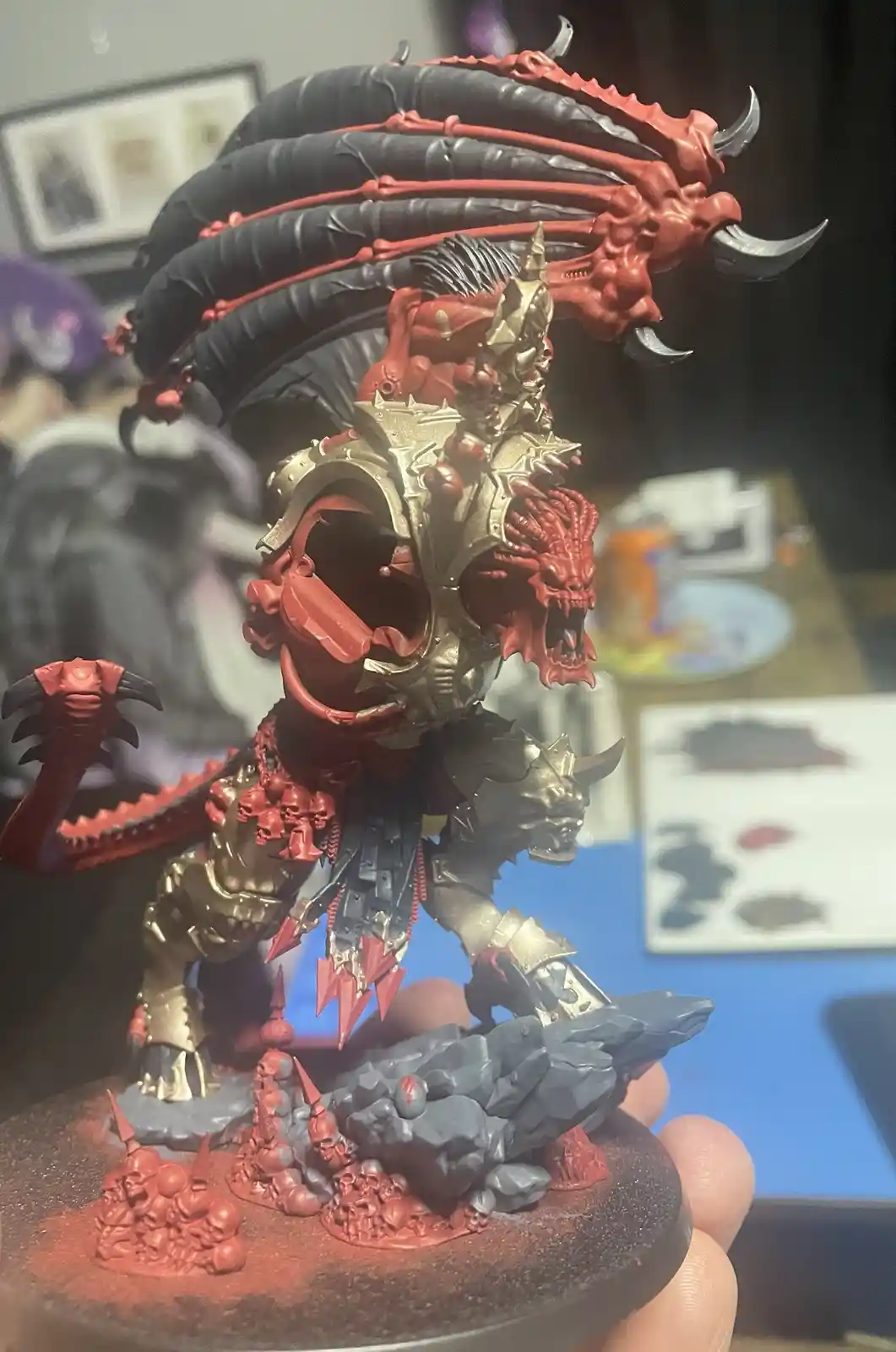 A highly detailed, hand-painted miniature of a demonic warlord with red and gold armor, multiple skulls, and a large black…