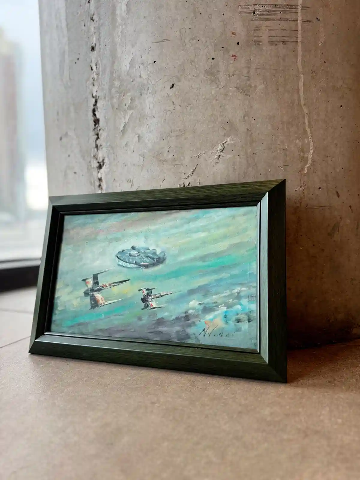 A small framed painting of Star Wars ships, including the Millennium Falcon and X-wings, is propped against a concrete…