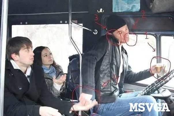 A man in a black beanie and jacket sits in the driver's seat of a bus, holding a cup, while two passengers sit in the front…