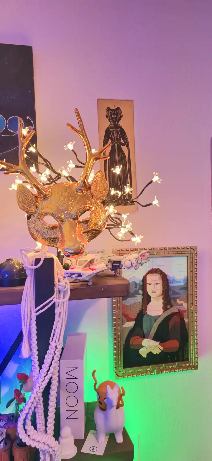A golden deer mask with glowing string lights shaped like antlers is displayed on a shelf next to a LEGO recreation of the…