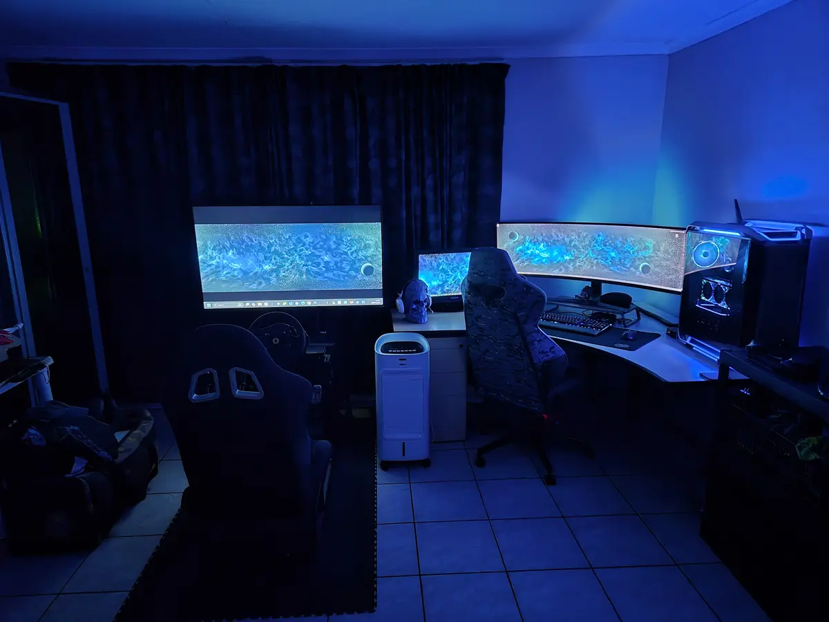 A dimly lit room bathed in blue light features a gaming setup with multiple monitors displaying a fish tank wallpaper, a…
