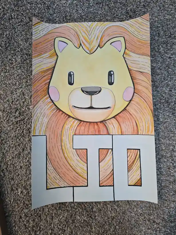 A hand-drawn cartoon lion with a yellow face, pink cheeks, and a large orange mane is depicted on paper, with the letters…