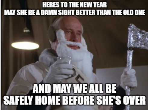 A man in a white hazmat suit with a fake white beard and goggles holds a glass and a foil-wrapped axe while looking solemn…