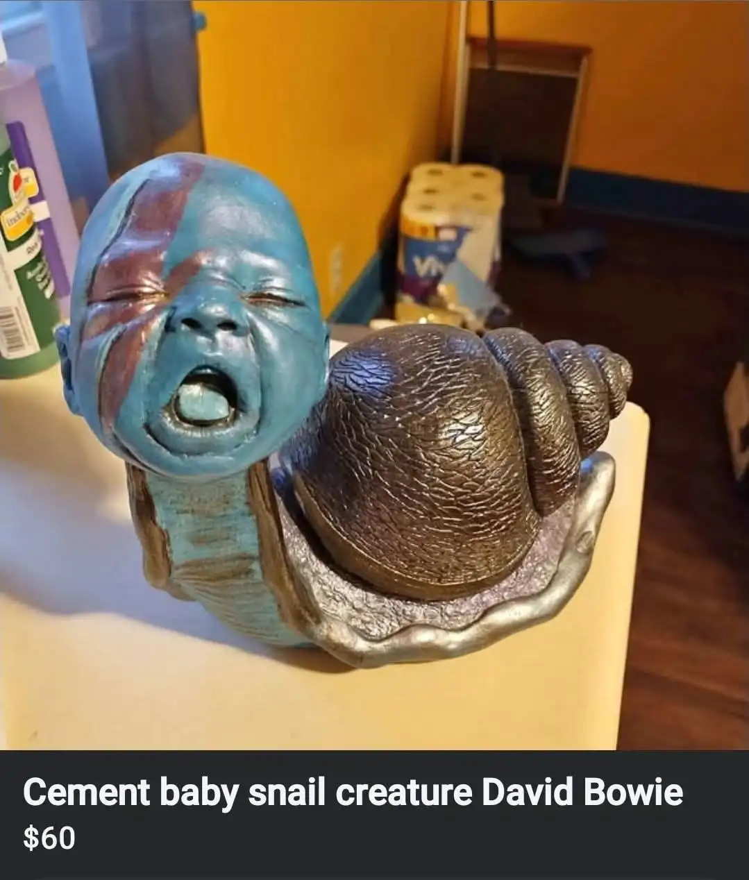 A figurine of a baby with blue skin and a red streak on its face, crying with its mouth open, is attached to a large…