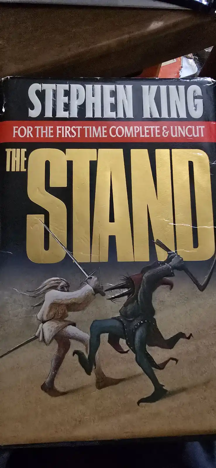 The image shows the cover of Stephen King's book 'The Stand', featuring two figures in a sword fight. The cover text reads…