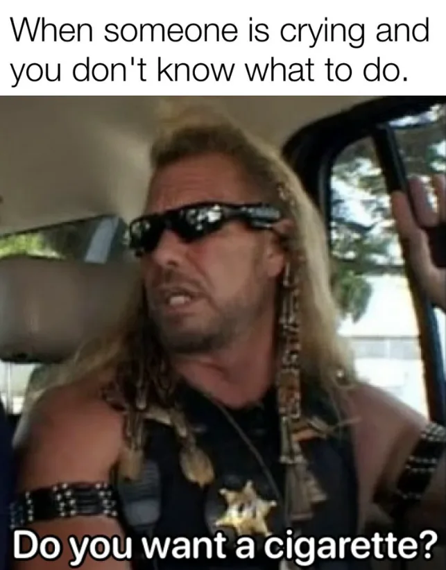 A man with long blonde hair, sunglasses, and a sheriff's star badge on his vest is inside a vehicle, looking concerned and…