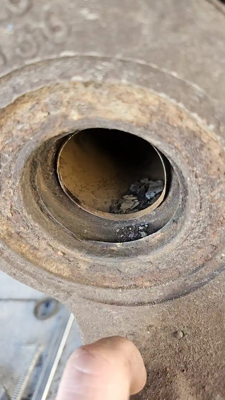 A close-up photo shows a rusty, circular opening in a metal grill component, with dark debris and ash visible inside. A…