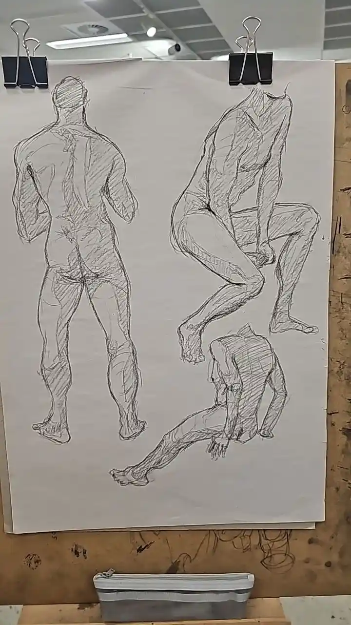 A sheet of paper clipped to an easel displays three rough pencil sketches of male nudes in different poses: standing…