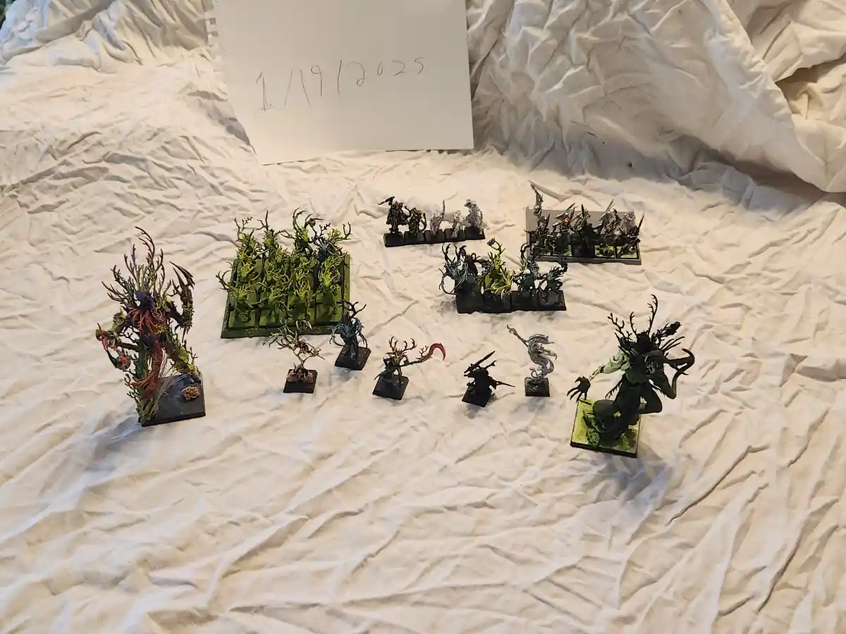 A collection of painted fantasy miniatures, including grotesque tree-like creatures and warriors, are arranged on a wrinkled…