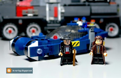 A photograph of two lego minifigures, one dressed as batman and the other as harry potter, standing in front of a blue lego…