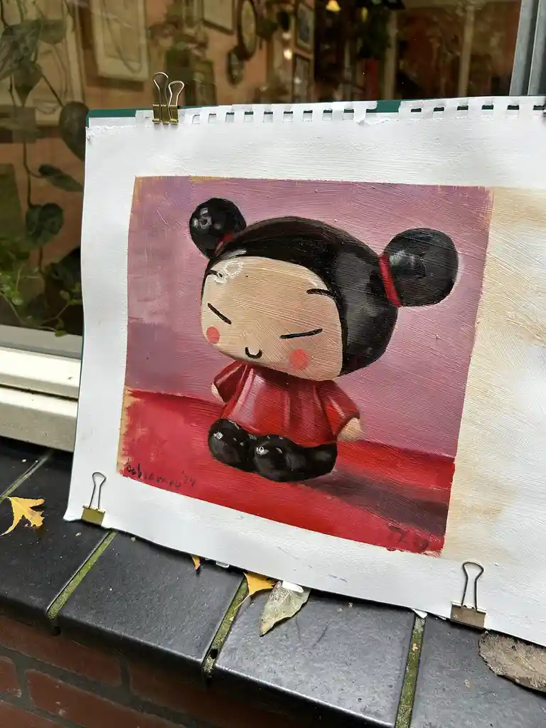 A painting of a cartoonish, chubby character with black pigtails, red cheeks, and a red outfit, sitting with closed eyes on…