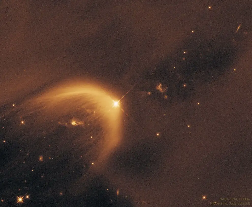 A Hubble Space Telescope image shows a bright star illuminating a glowing, curved nebula against a dark cosmic background…