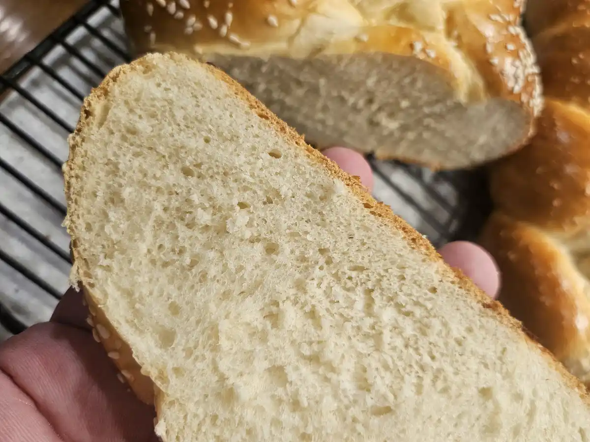 A close-up photo shows a hand holding a freshly sliced loaf of bread, revealing its soft, porous interior. In the…