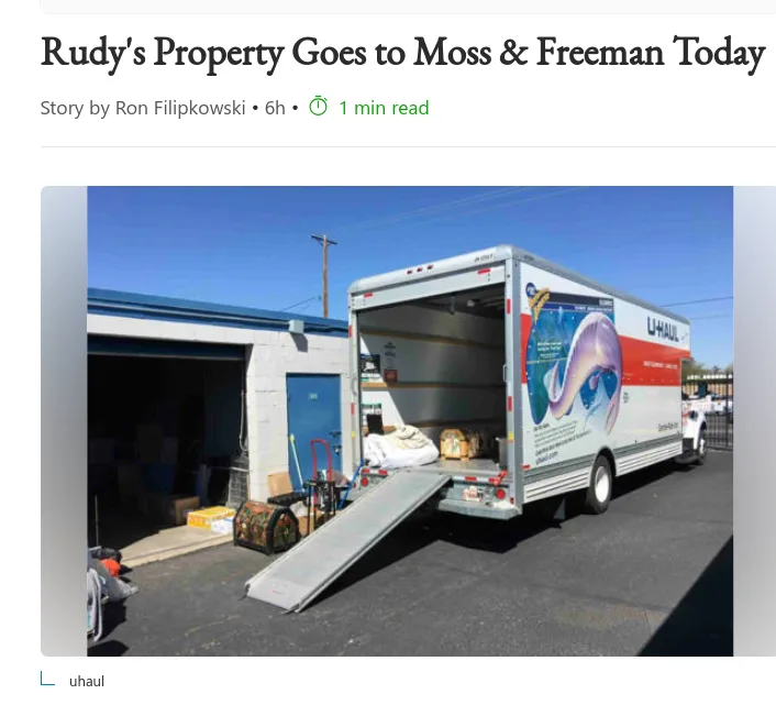 A U-Haul moving truck with its back door open and ramp extended is parked outside a building, loaded with various items…