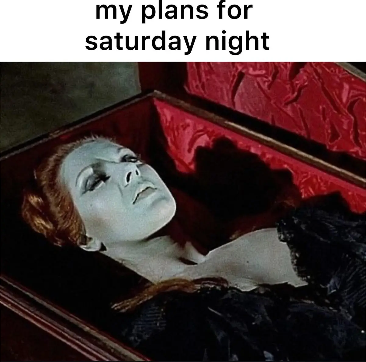 A still image from a horror film shows a pale, blue-faced woman with red hair lying in an open coffin lined with red velvet…
