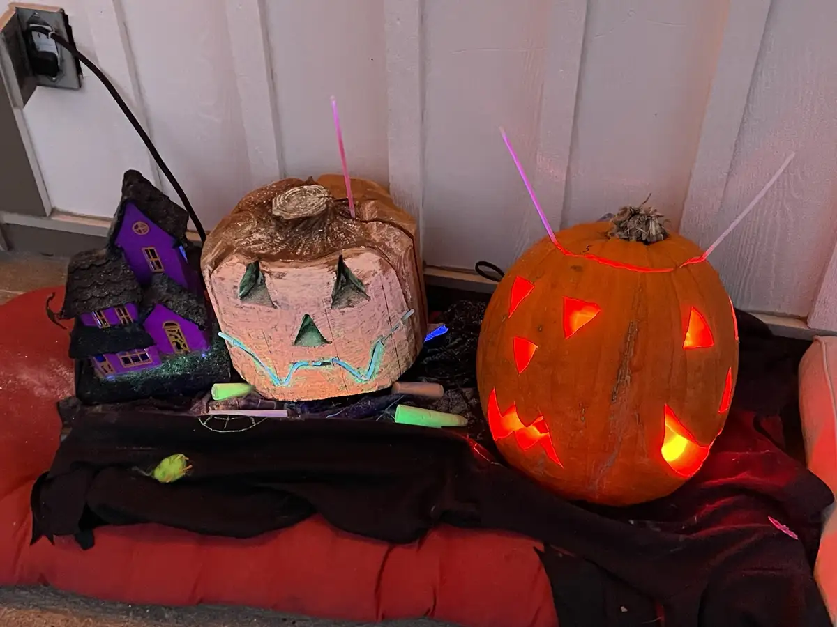 Two Halloween decorations sit on a red cushion: a traditional orange jack-o'-lantern with glowing eyes and a carved face…