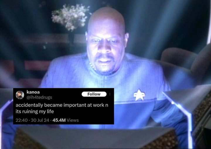 A screenshot of a Star Trek: The Next Generation scene featuring a bald man in a blue uniform with a star insignia, looking…