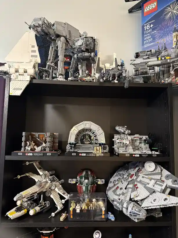 A dark wooden shelf displays multiple large, intricate LEGO Star Wars sets, including an AT-AT walker, Millennium Falcon…