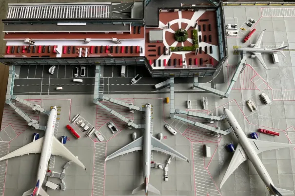 An overhead view of a detailed model airport with three large passenger jets parked at gates, surrounded by miniature ground…