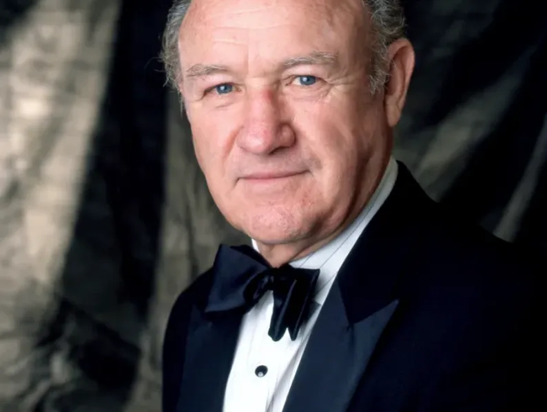 a close-up portrait of actor Gene Hackman wearing a black tuxedo with a bow tie and white shirt, looking directly at the…