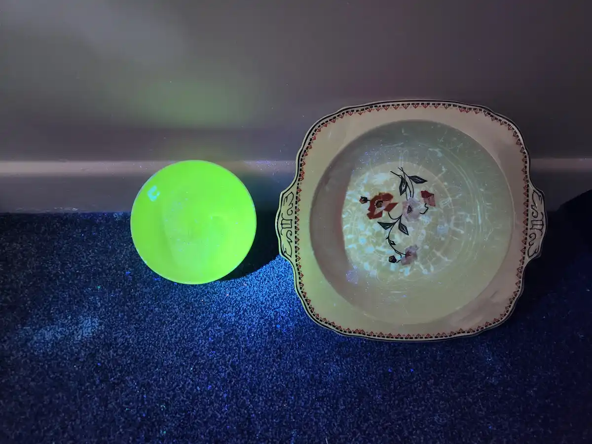 A small, bright green glowing bowl sits next to a larger, ornate ceramic bowl with floral patterns, both resting on a dark…