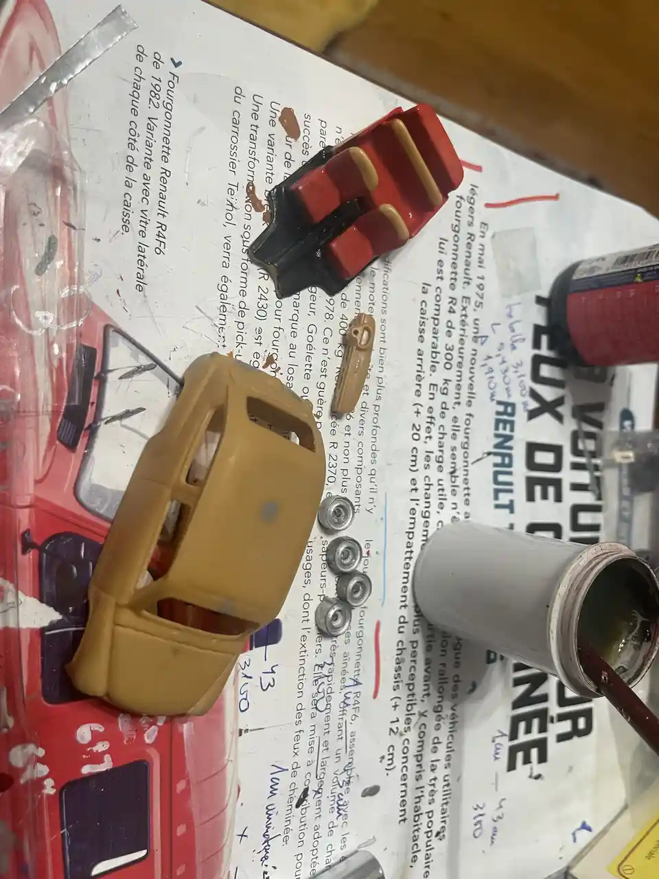 A close-up photo shows a partially painted yellow plastic toy car body and a red-and-black plastic car roof piece on a work…