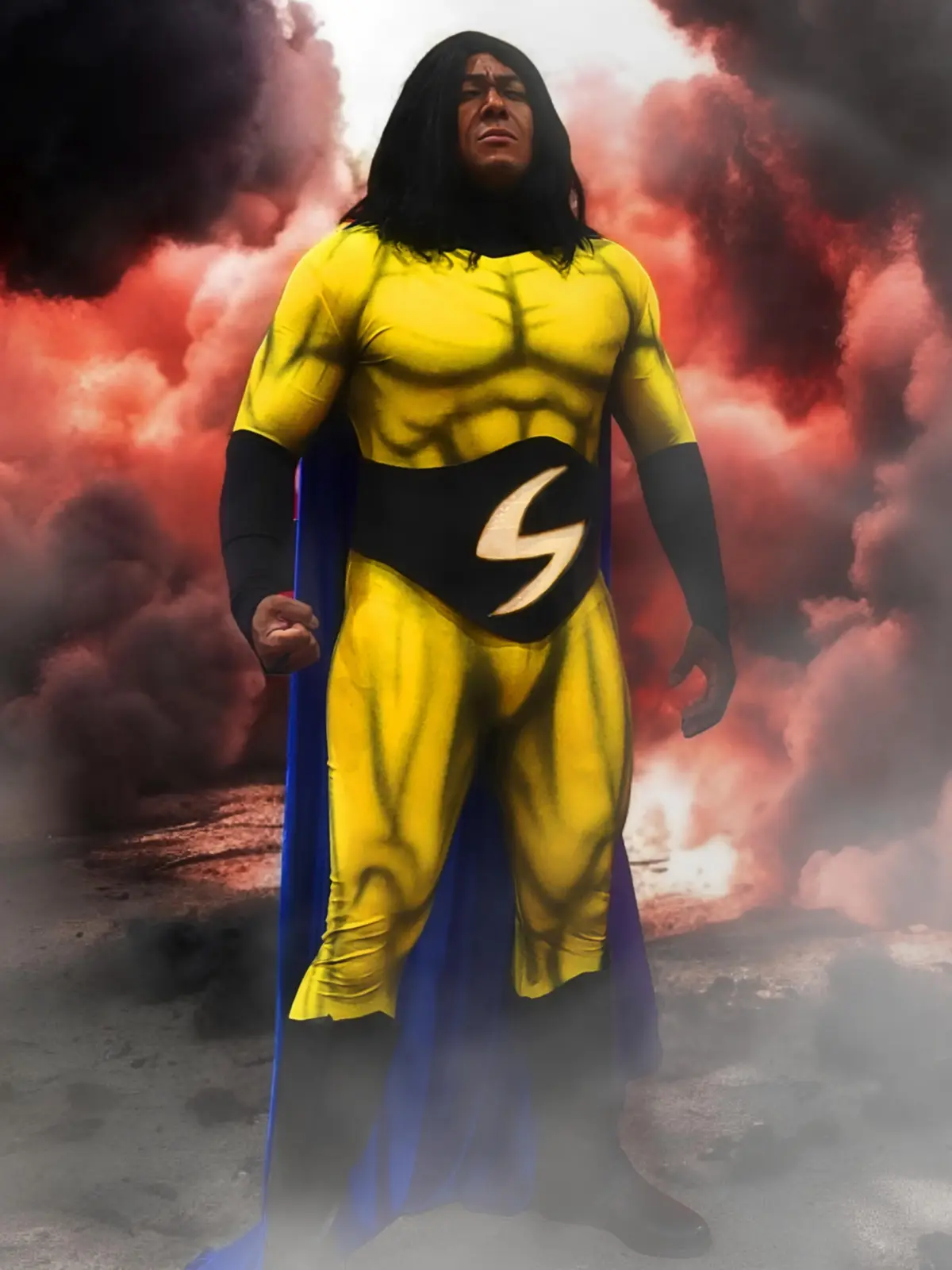 A man in a yellow superhero costume with a blue cape and a black belt featuring a lightning bolt stands against a dramatic…