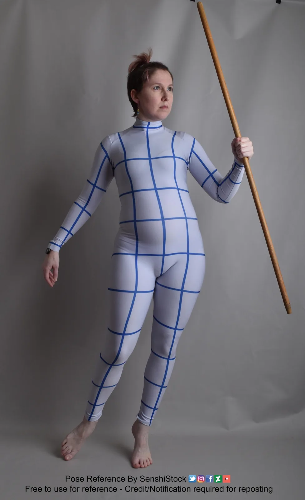 A person stands in a studio against a plain gray backdrop, wearing a form-fitting white bodysuit with a blue grid pattern…