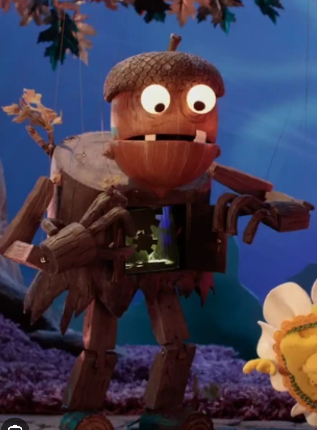A wooden puppet character with an acorn head, large white eyes, and twig limbs stands in a forest setting, holding a glowing…