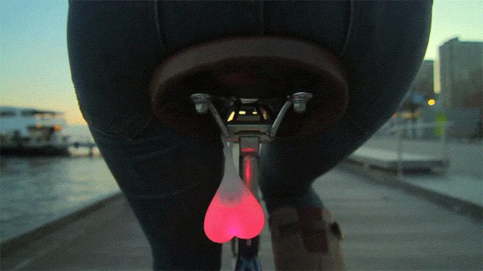 A six-panel image shows a close-up of a person's rear end on a bicycle, with a glowing pink heart-shaped light attached to…