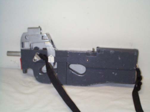 a close-up photo of a dark gray, homemade-looking firearm with a black strap attached, resting on a white surface against a…