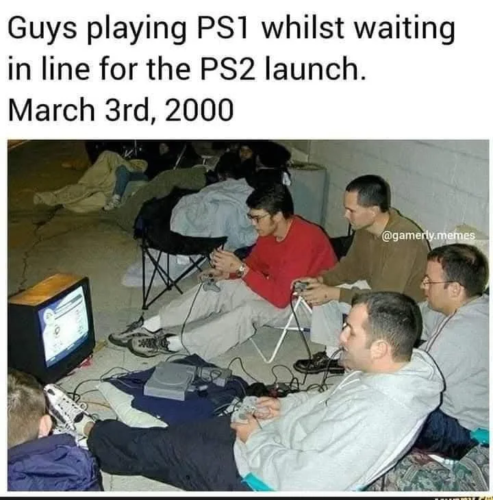 Several men are sitting on folding chairs on a concrete floor, playing PlayStation 1 games with controllers, while waiting…