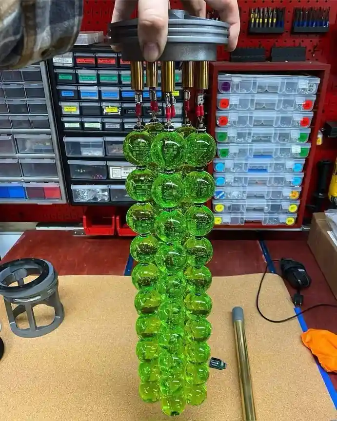 A person holds a tall, green, spherical object resembling a Christmas tree, constructed from numerous transparent green…