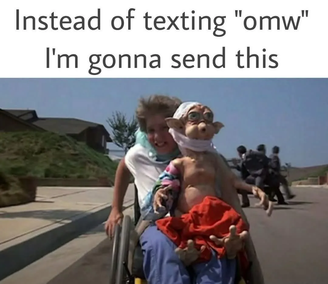 A young child in a wheelchair is smiling while holding a small, bandaged, alien-like creature with large eyes and pointed…