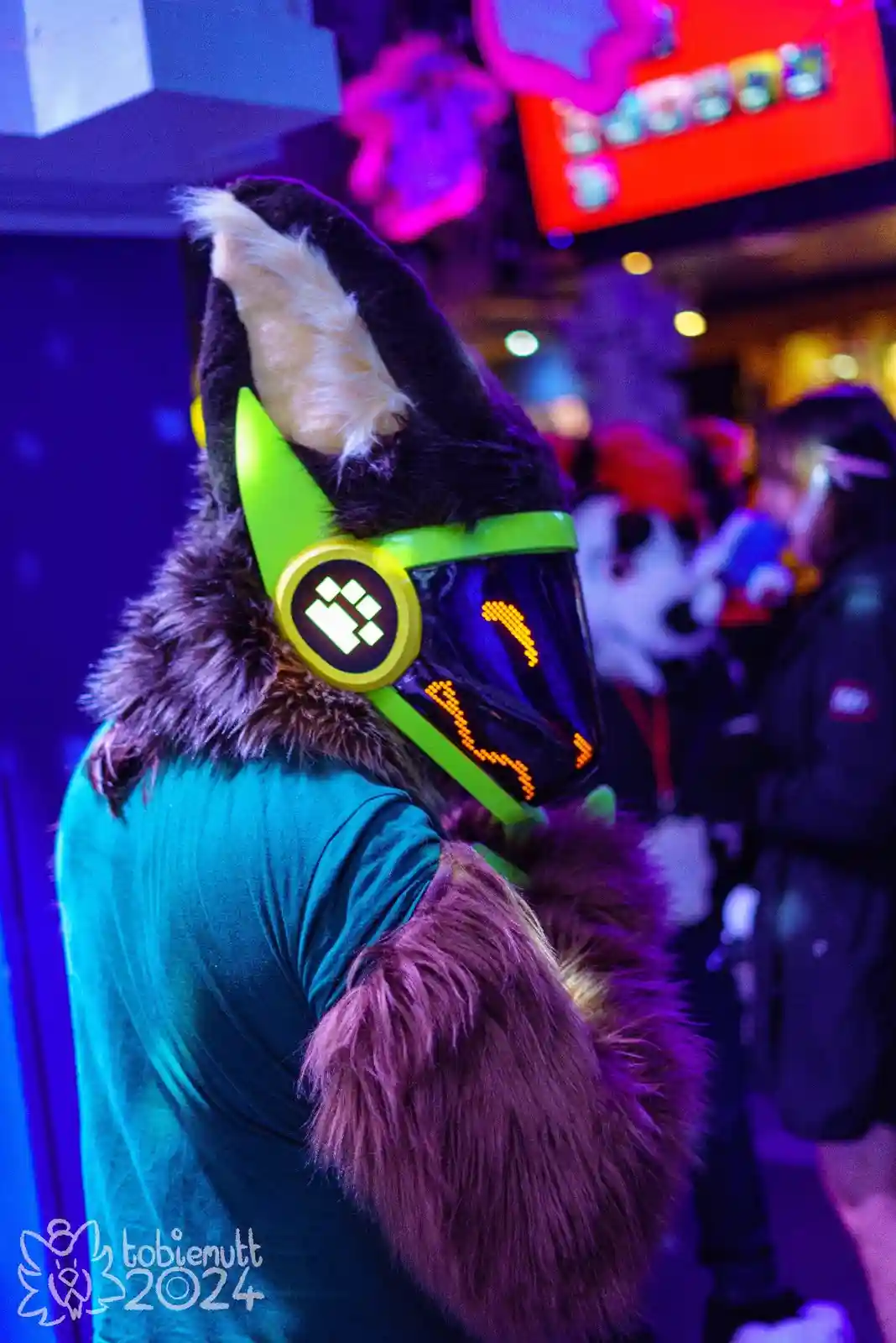 A person in a furry animal costume with a glowing green headset and a digital display showing a sad face is seen from behind…