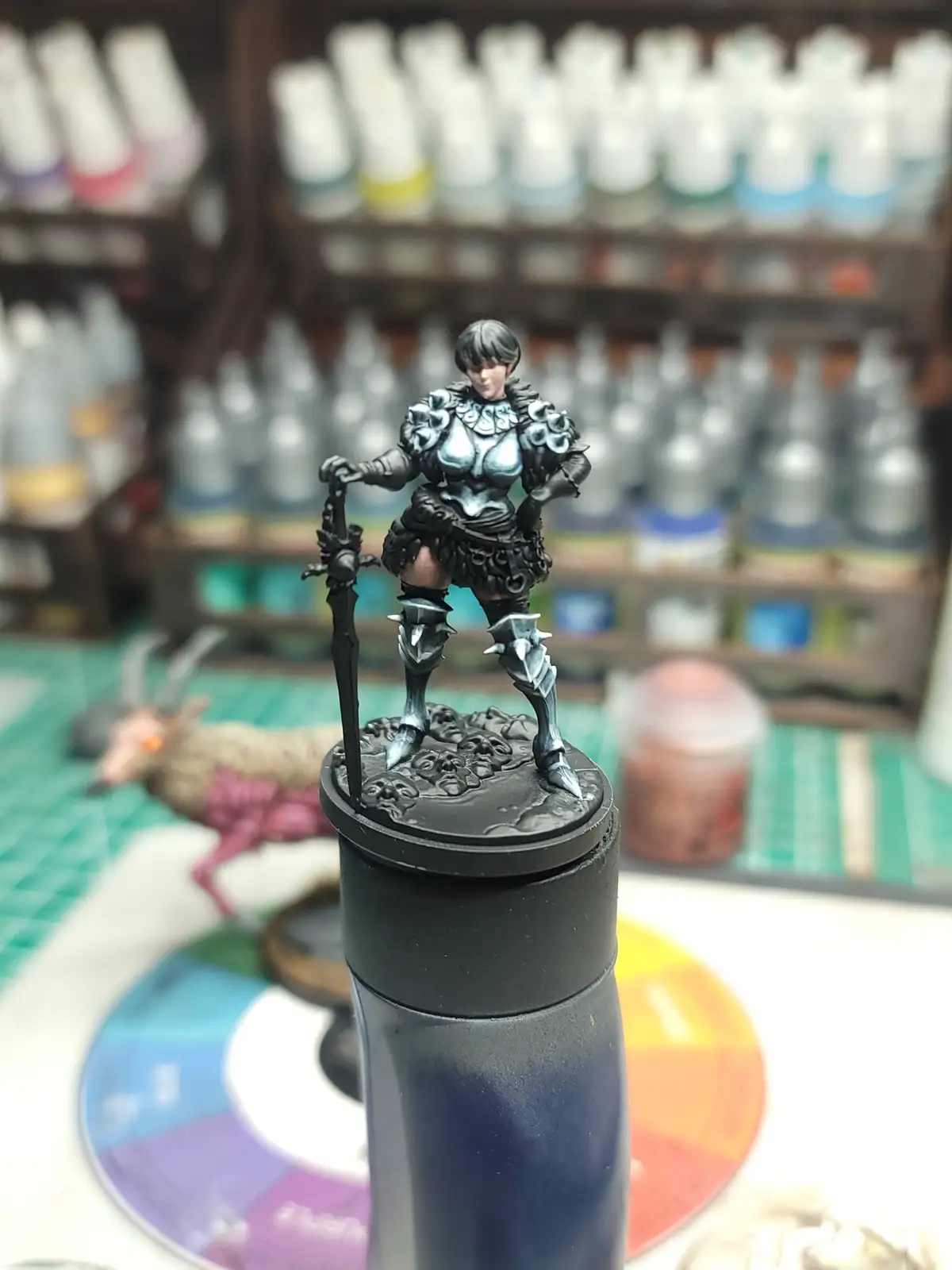 A painted fantasy miniature of a female warrior in ornate armor stands on the cap of a dark blue water bottle, holding a…